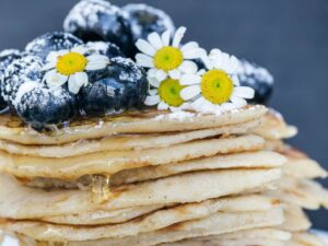 Stack of pancakes topped with blueberries, daisies, and syrup, close-up shot.