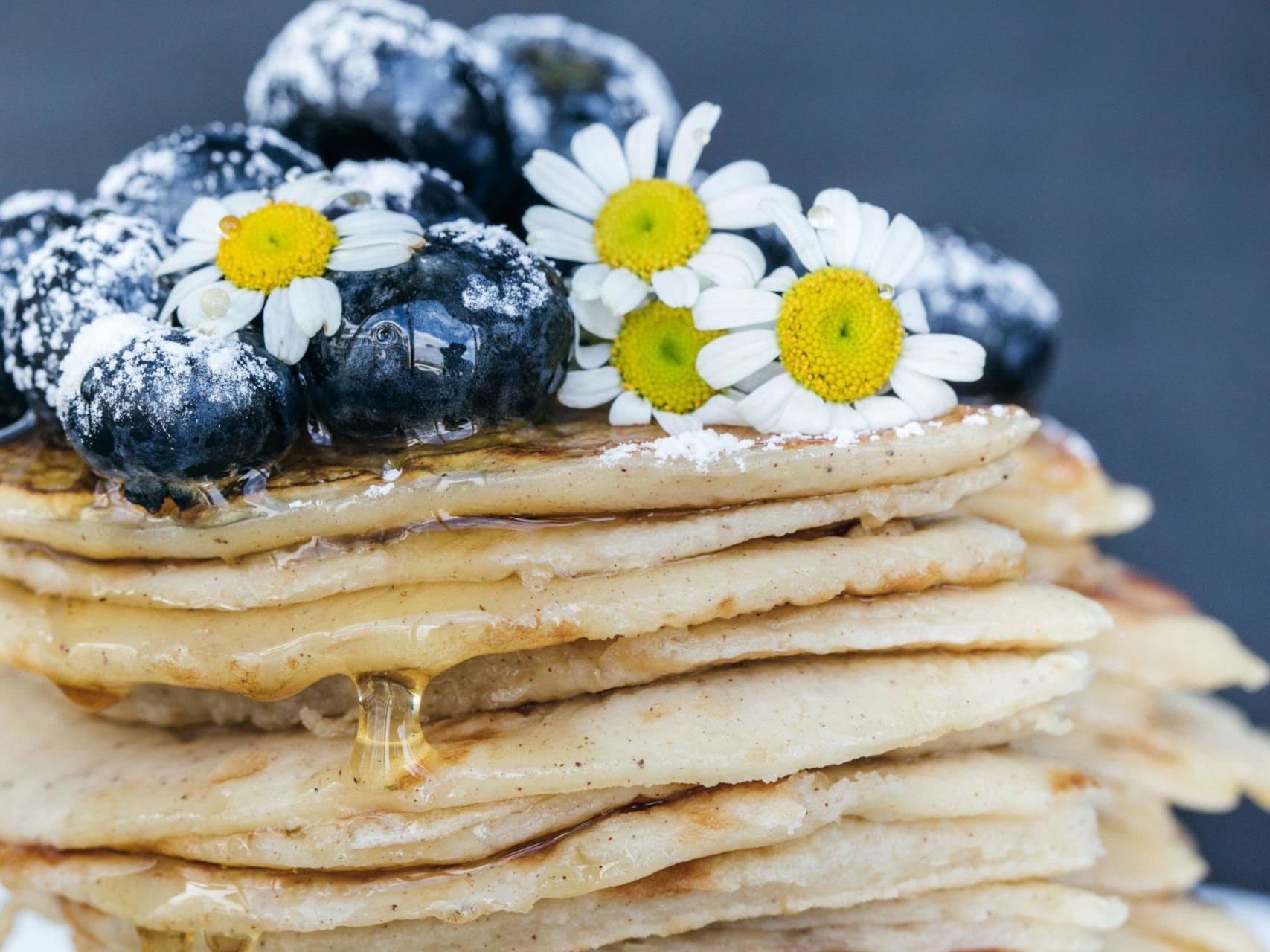 Stack of pancakes topped with blueberries, daisies, and syrup, close-up shot.