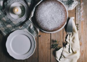 Chocolate cake dusted with powdered sugar on a rustic wooden table with plates and utensils.