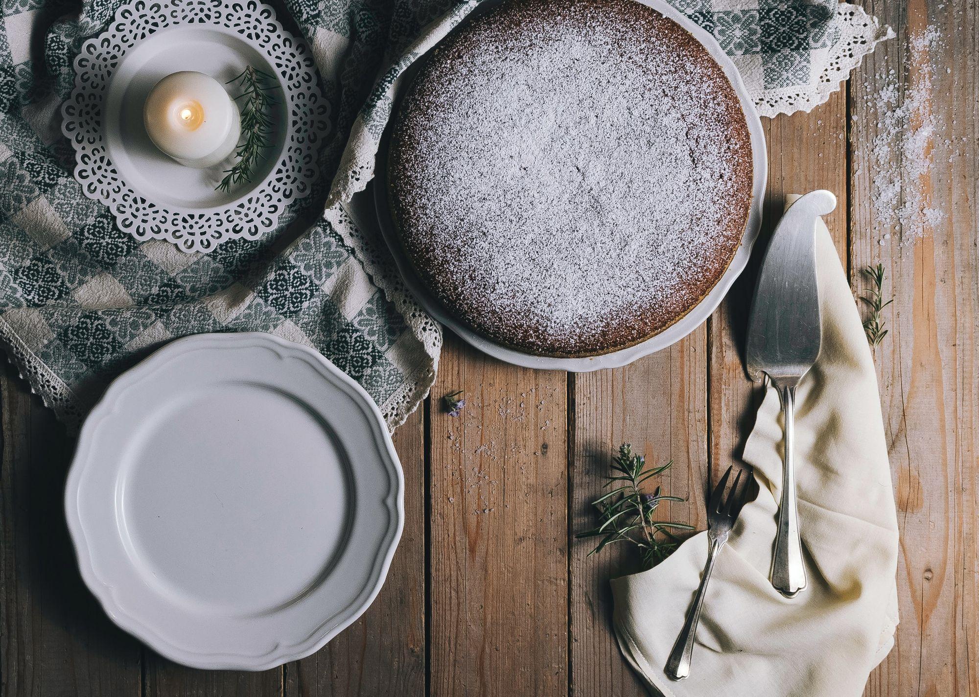 Chocolate cake dusted with powdered sugar on a rustic wooden table with plates and utensils.