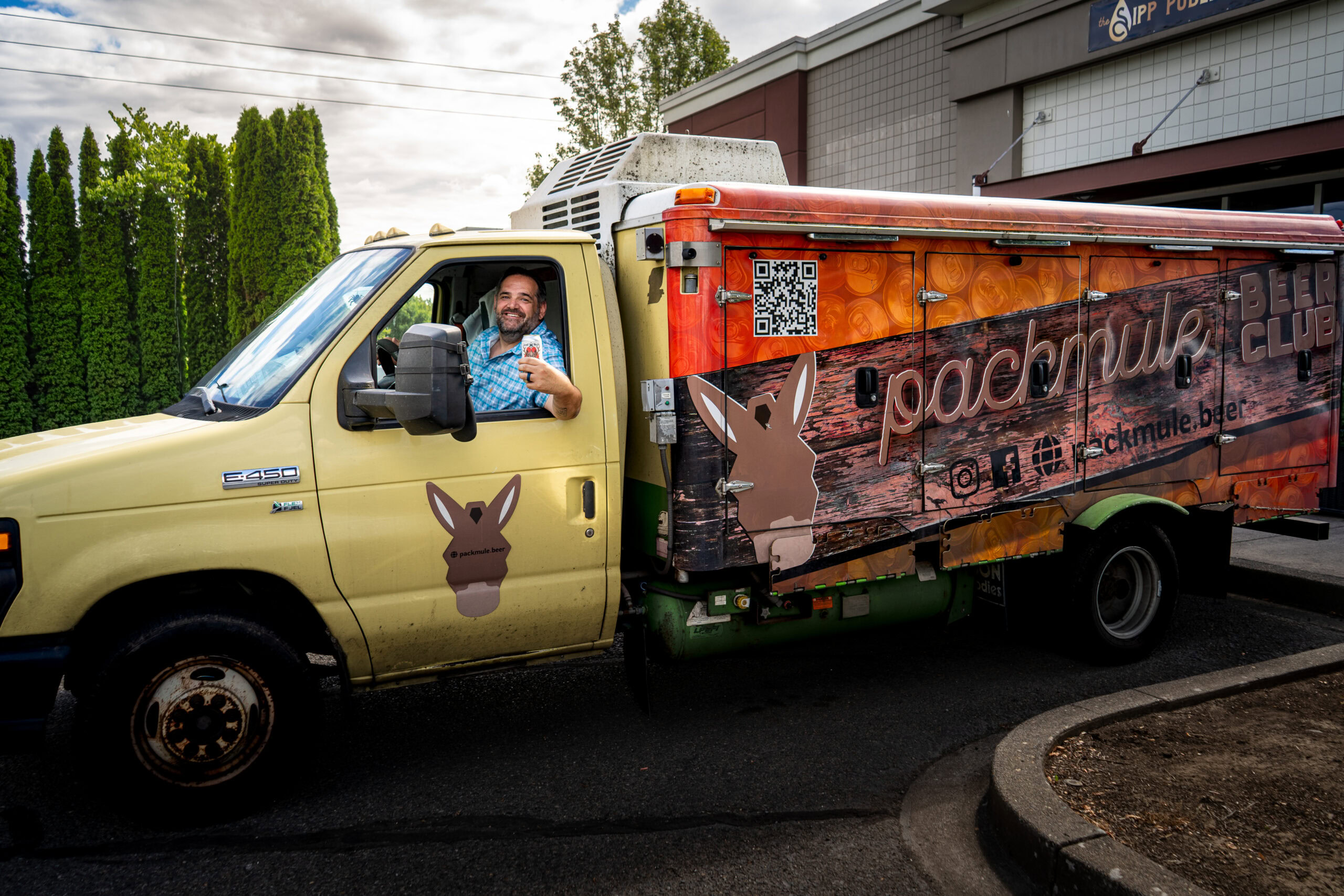 Delivery truck with rabbit logo and advertising for packmule.ursa6.com, driven by a smiling man in a blue checkered shirt.