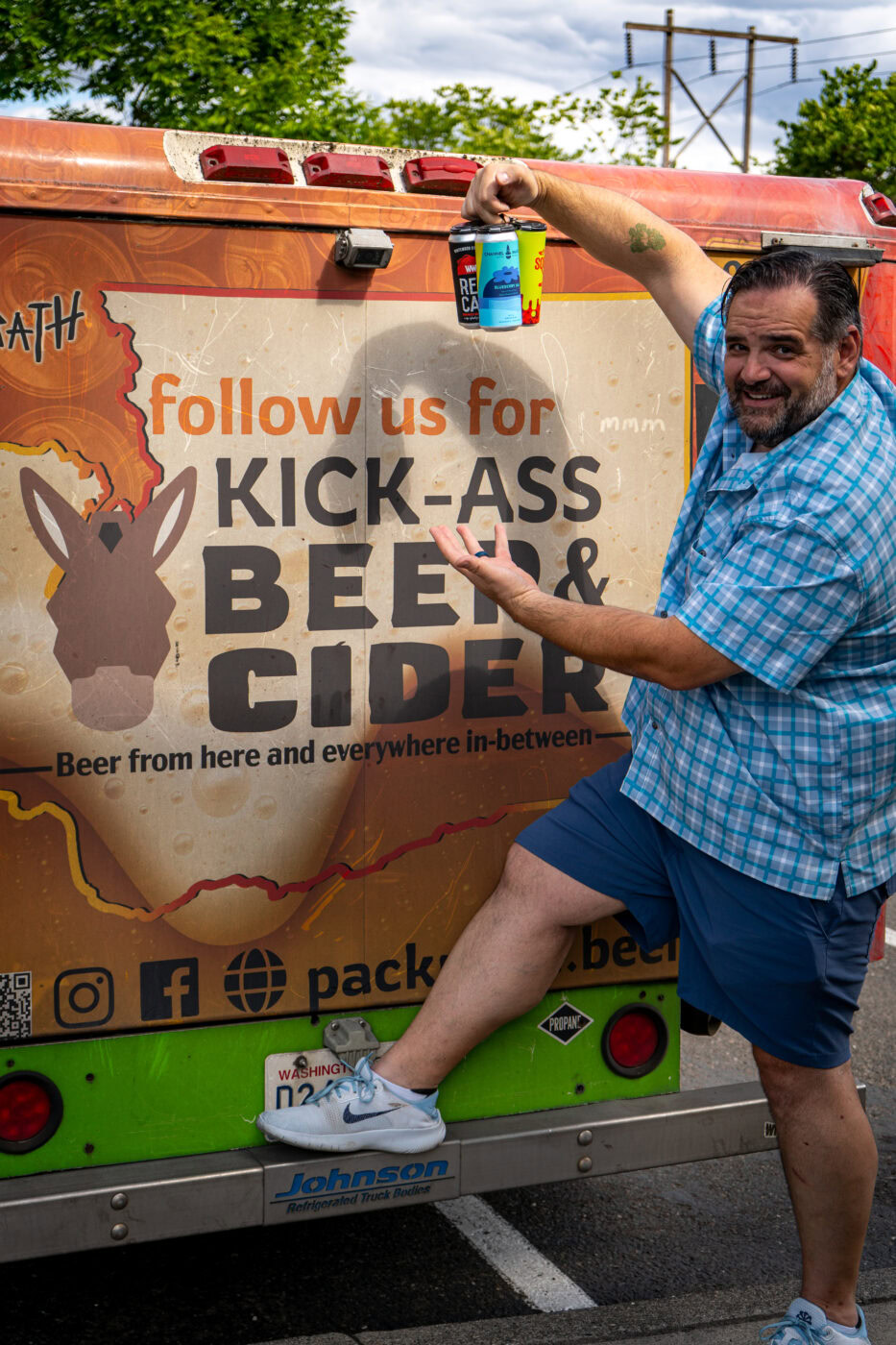 Happy man holding a beer can next to a promotional van for beer and cider festival.